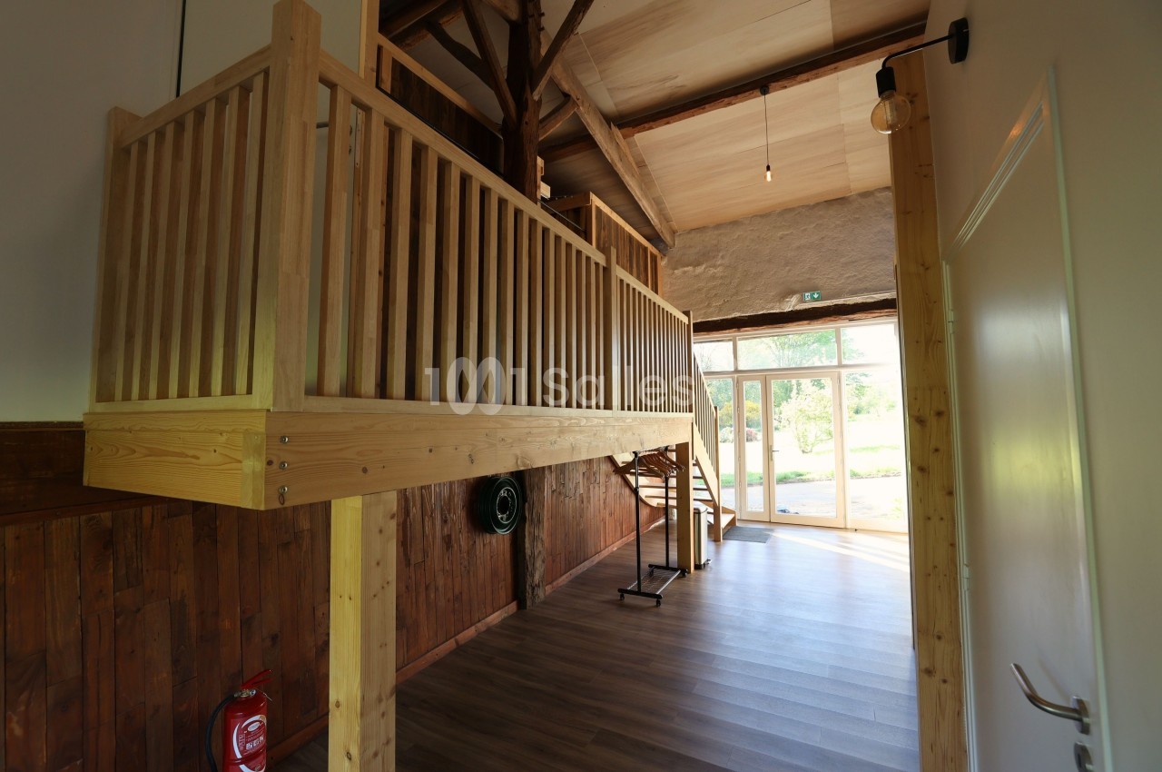 Mezzanine en bois dans un intérieur lumineux avec murs en pierre et parquet, vue sur une porte vitrée donnant sur l…