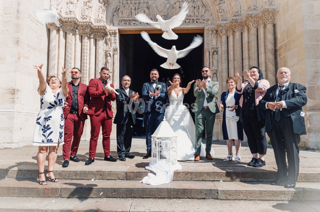 Un couple de mariés et leurs invités devant une église libèrent des colombes en signe de célébration.