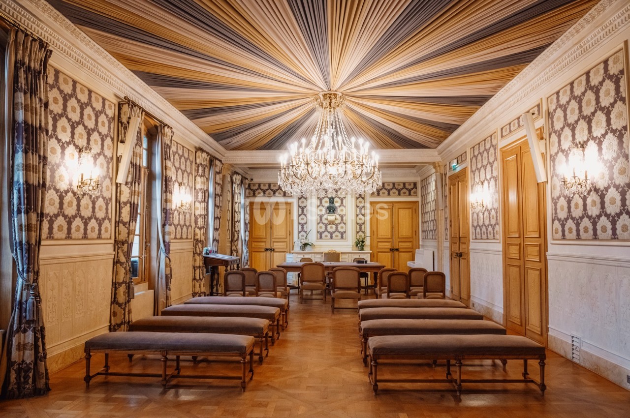 Salle élégante avec plafond rayé, lustre imposant, bancs alignés et murs ornés de motifs décoratifs.