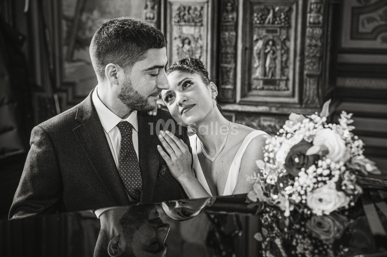 Un couple habillé élégamment partage un moment tendre près d'un piano, avec un bouquet de fleurs en avant-plan.