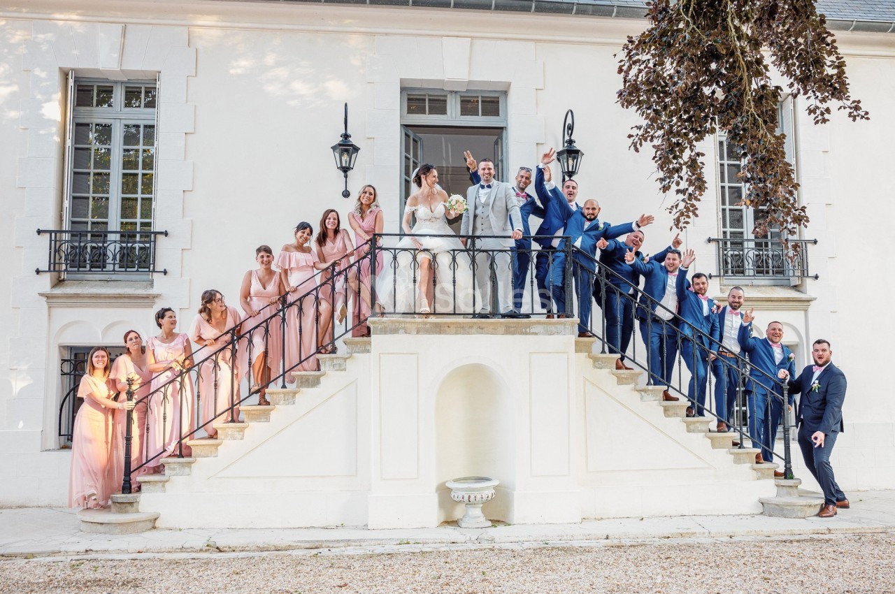 Groupe de personnes posant sur un escalier devant une grande maison blanche, lors d'une cérémonie festive.
