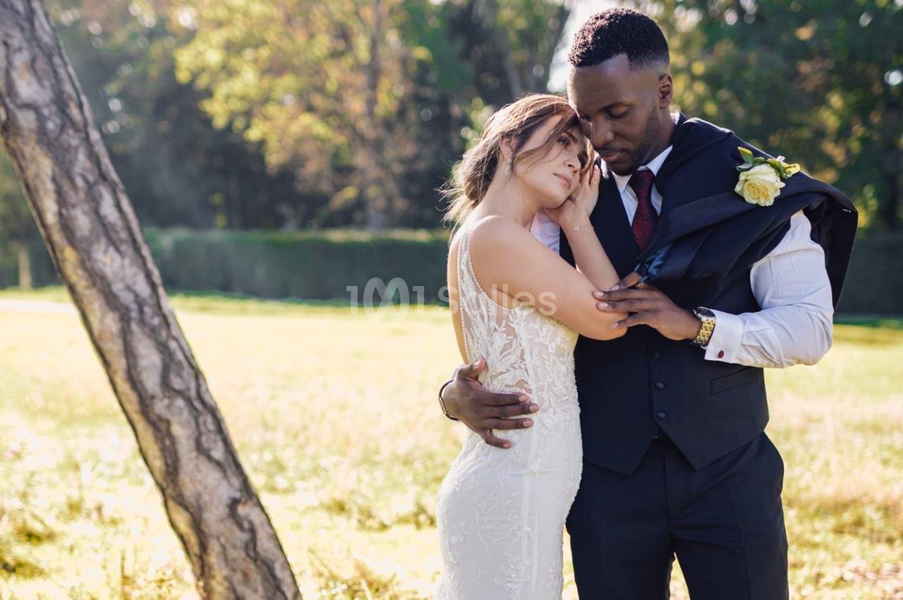 Un couple en tenue de mariage s'enlace tendrement dans un parc ensoleillé, entouré de verdure.