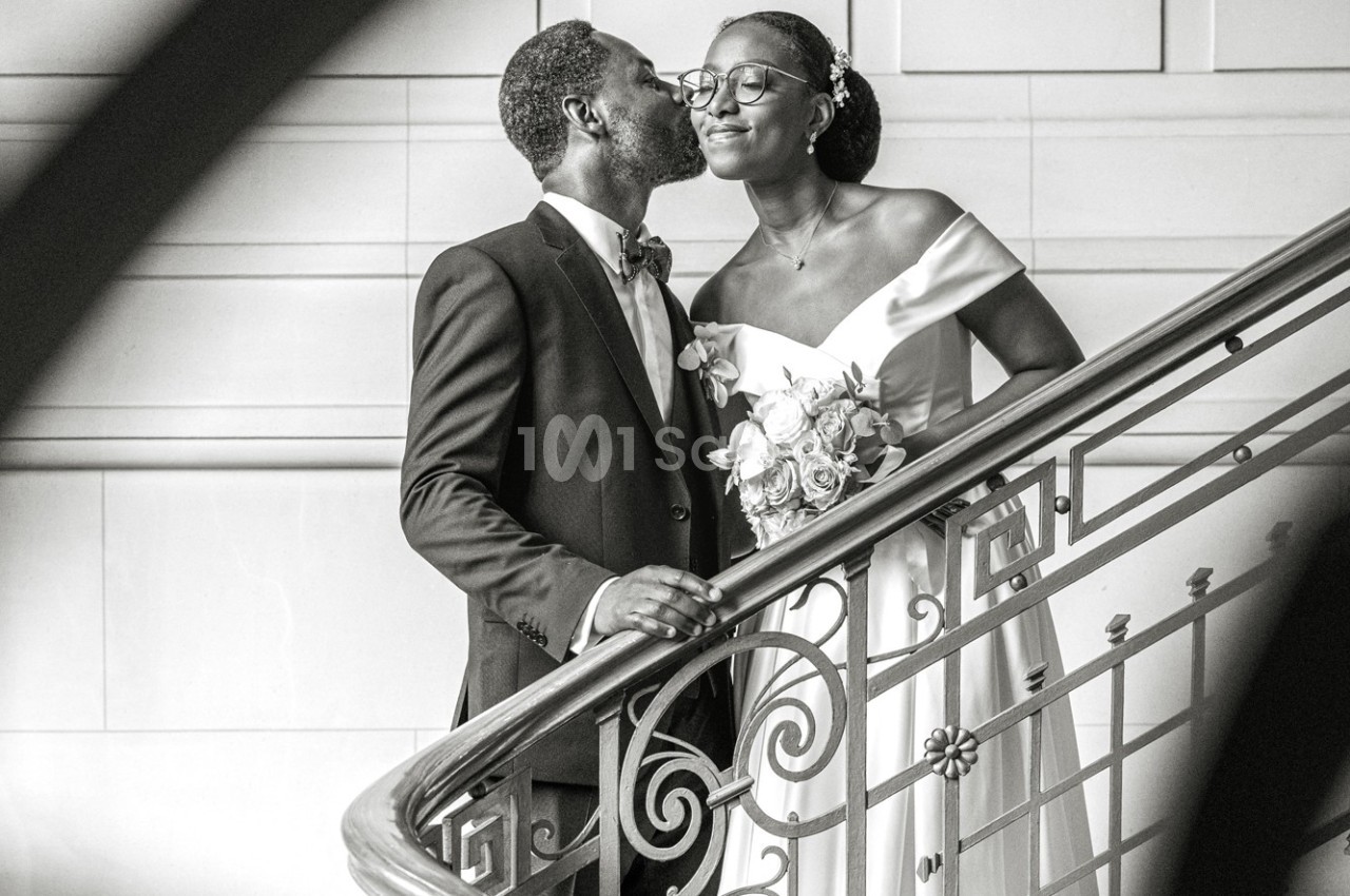 Un couple habillé élégamment partage un moment complice sur un escalier en intérieur.