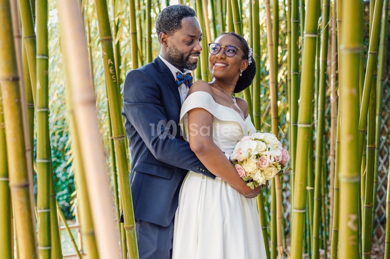 Un couple en tenue de mariage pose dans une forêt de bambous, la mariée tenant un bouquet de fleurs.