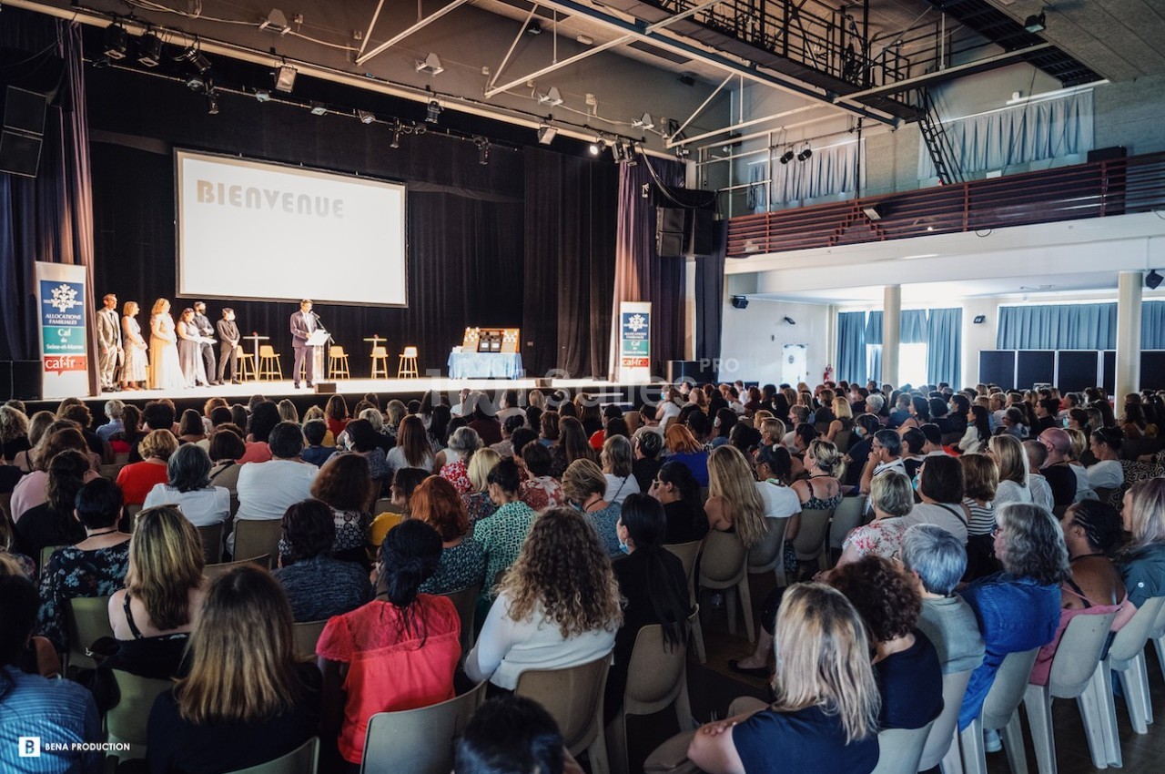 Une assemblée de personnes assises dans une salle de spectacle, face à une scène où se tient une présentation.