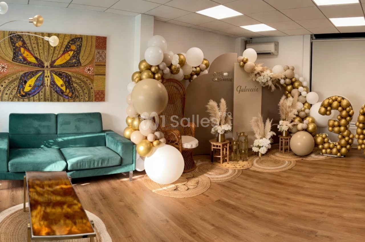 Décoration intérieure avec ballons dorés et blancs formant le chiffre 30, fauteuil en rotin et plantes en arrière-plan.