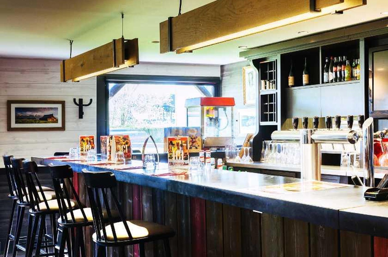 Bar en bois avec tabourets hauts, comptoir équipé de tireuses à bière, étagères avec bouteilles et décoration lumineuse.