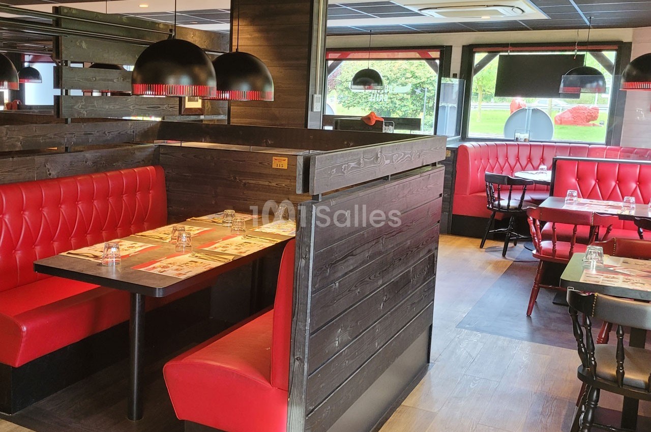 Salle de restaurant avec banquettes rouges, tables dressées et luminaires suspendus dans un décor en bois sombre.