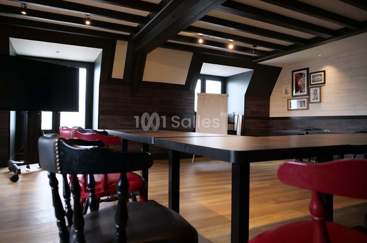 Salle de réunion lumineuse avec tables noires, chaises rouges et noires, tableau blanc et décorations murales.