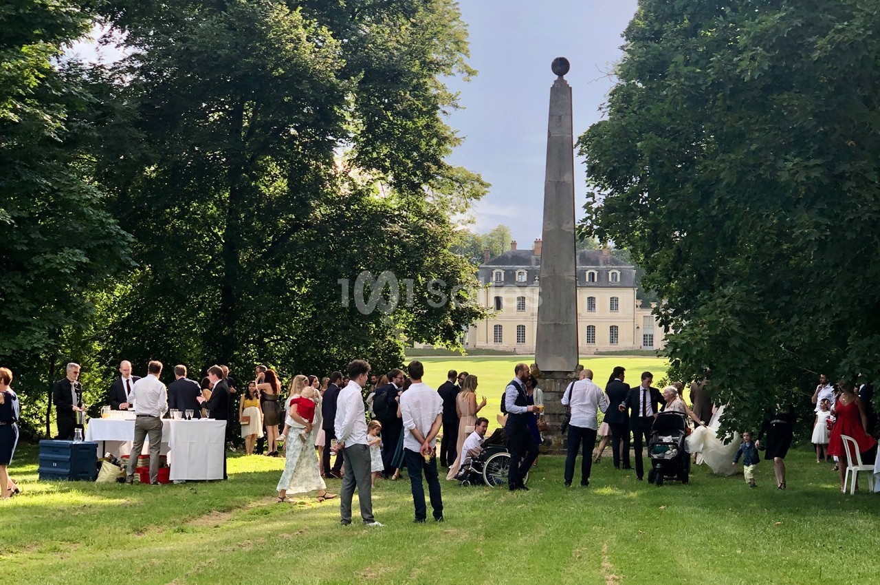 Groupe de personnes réunies dans un parc verdoyant près d'un obélisque, avec un château en arrière-plan.