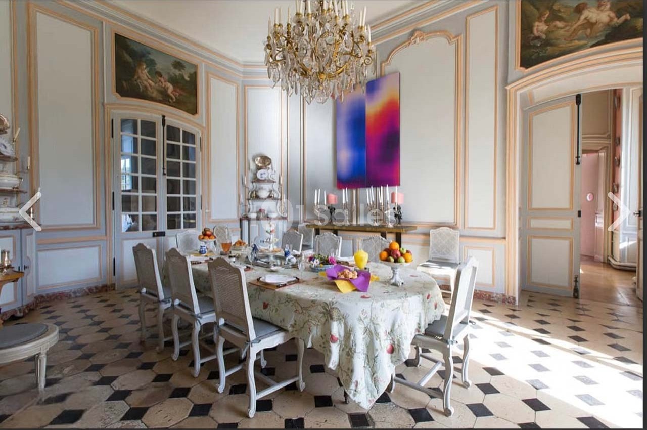 Salle à manger lumineuse avec table dressée, lustre en cristal, murs ornés et sol en carreaux noirs et blancs.
