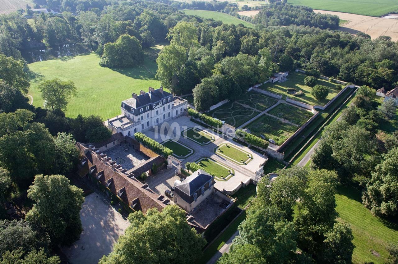Vue aérienne d'un château entouré de jardins symétriques, d'arbres et de vastes espaces verts en campagne.
