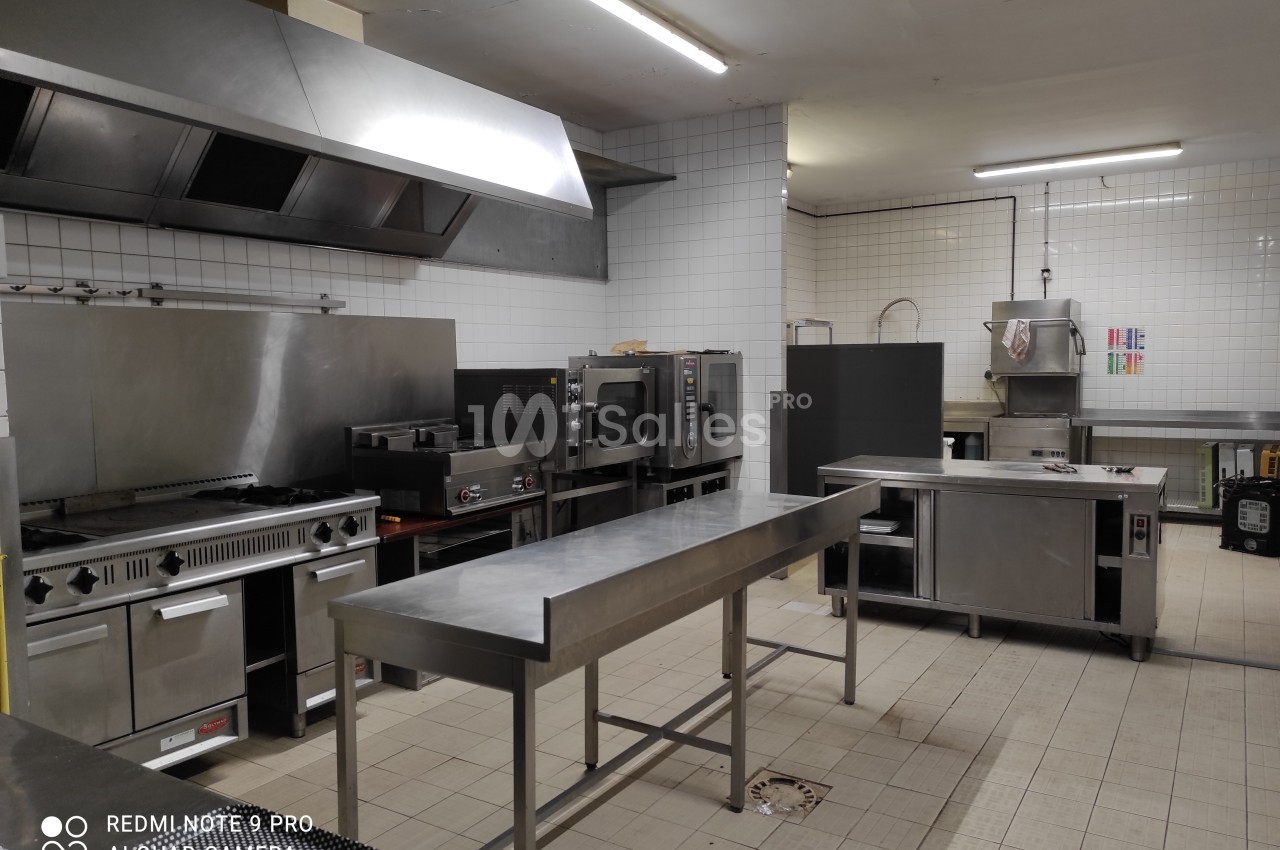 Cuisine professionnelle avec équipements en inox, comprenant fours, plaques de cuisson, plans de travail et évier.