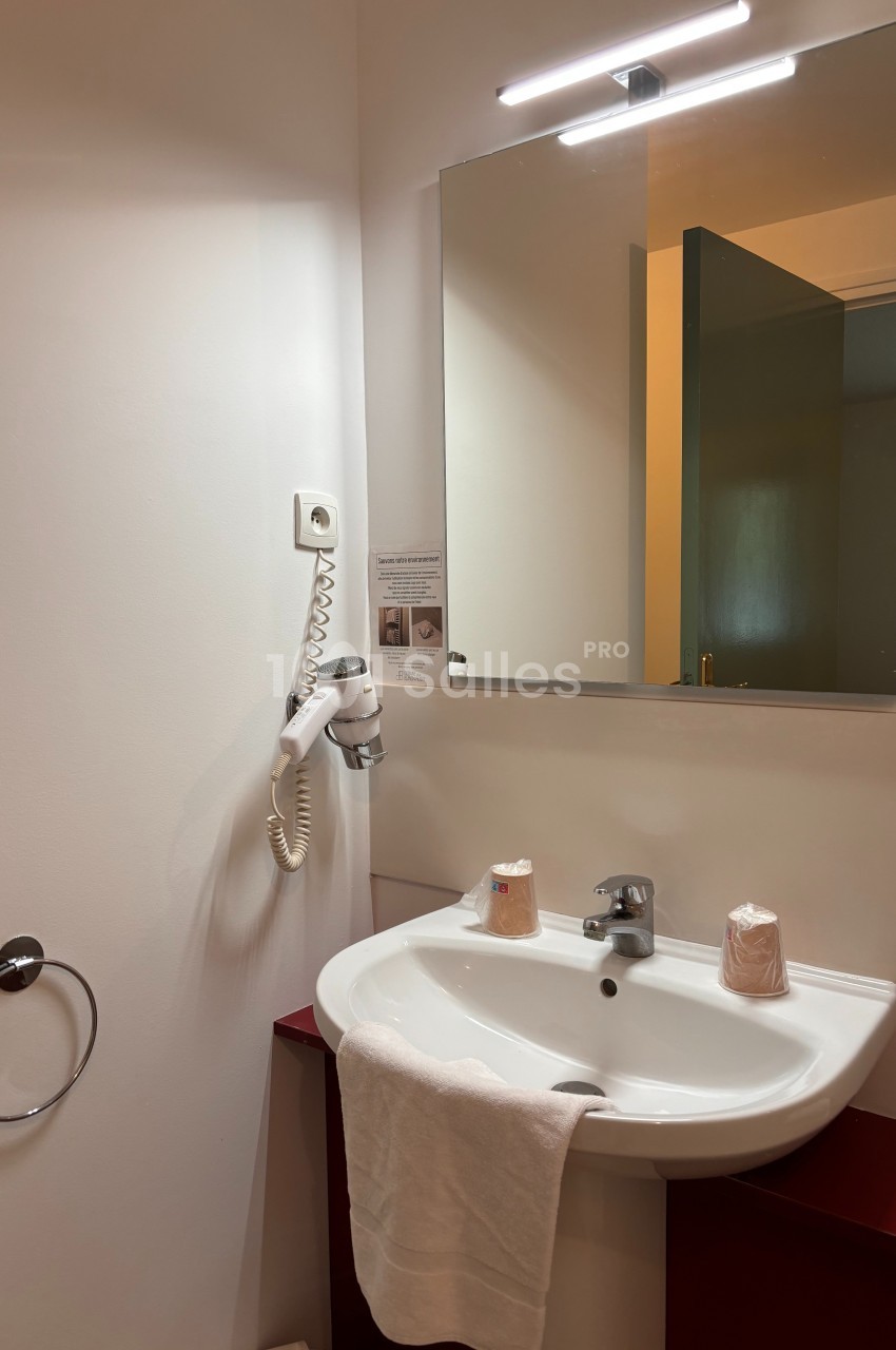 Lavabo blanc avec miroir éclairé, sèche-cheveux mural et serviette accrochée, dans une salle de bain sobre.