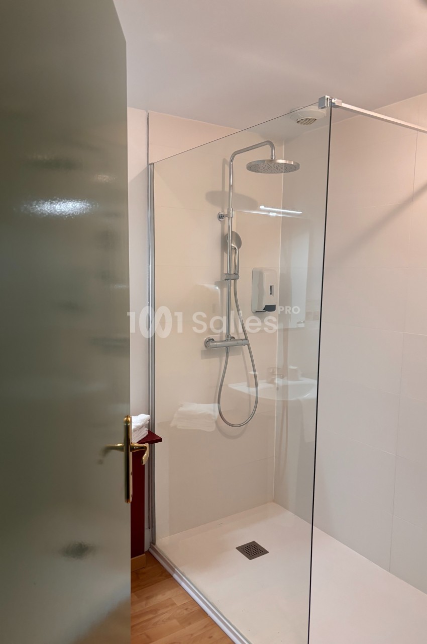 Douche moderne avec paroi en verre, pommeau de douche mural et sol en bois visible à l'extérieur.