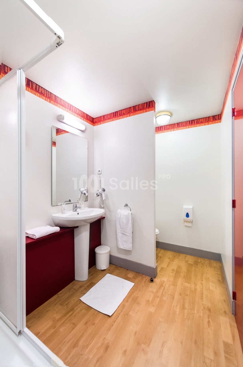 Salle de bain avec lavabo, miroir, serviette suspendue, sol en bois clair et éclairage au plafond.