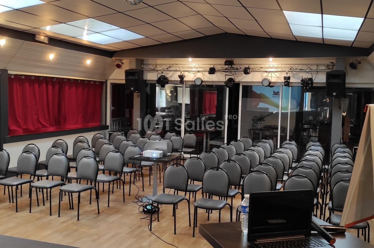 Salle de conférence équipée de chaises alignées, d'un projecteur, d'un tableau blanc et d'une scène avec éclairage.