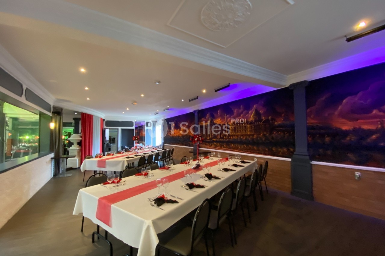 Salle de réception décorée avec des tables dressées, nappes blanches et rouges, et fresque murale en arrière-plan.
