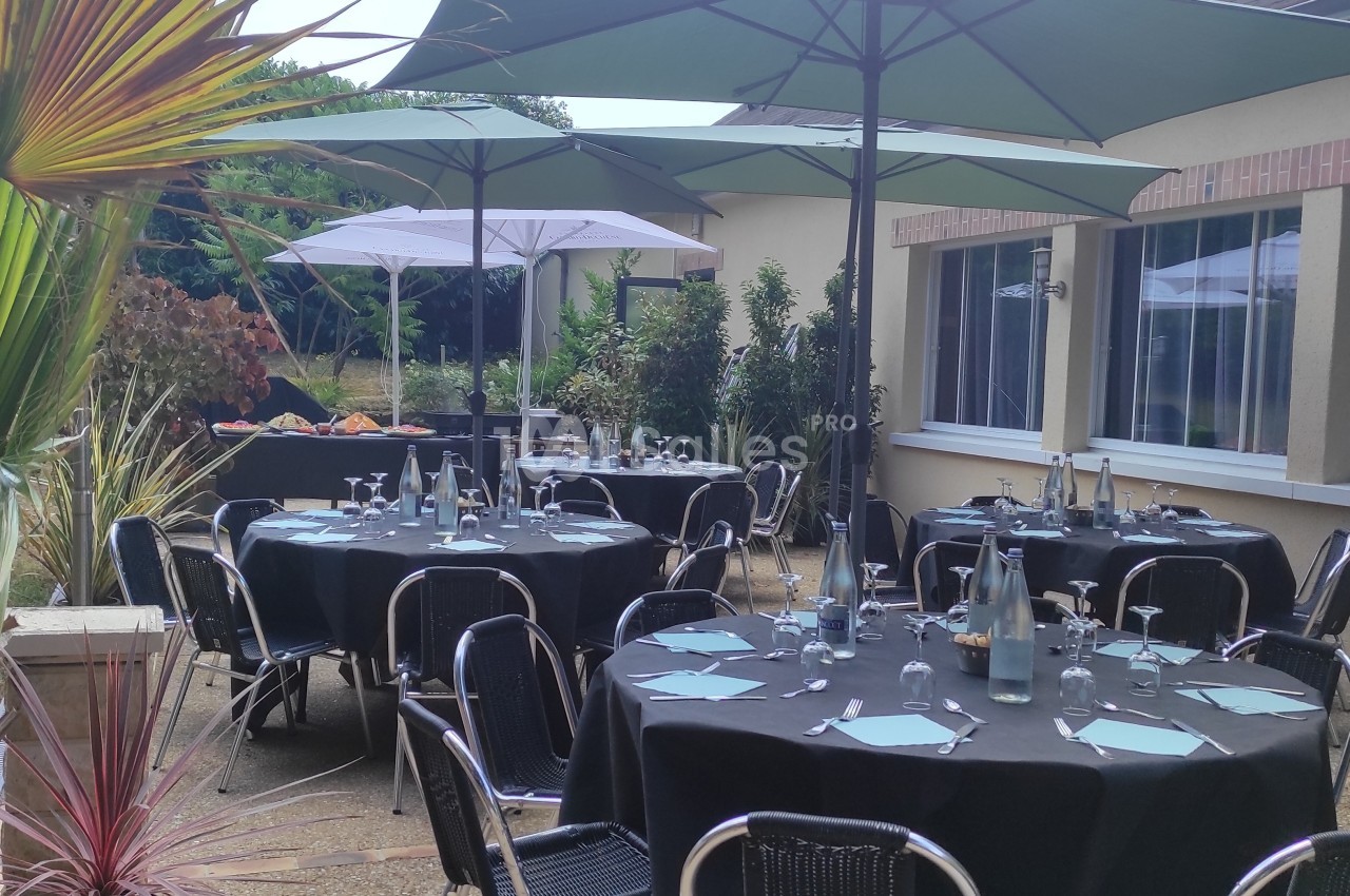 Terrasse aménagée avec des tables rondes dressées, chaises noires et parasols, entourée de verdure.