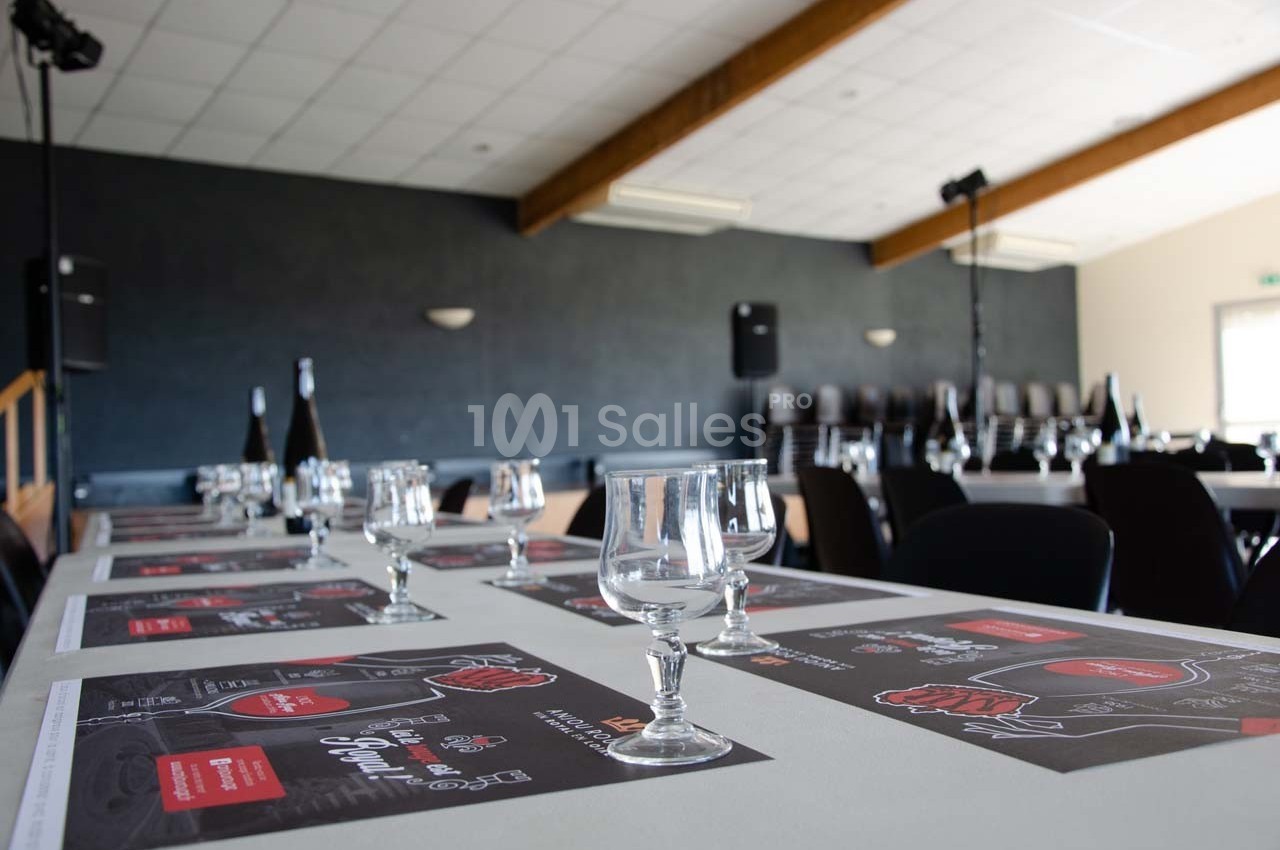 Salle de réception avec tables dressées, verres et menus, éclairée par une lumière naturelle.