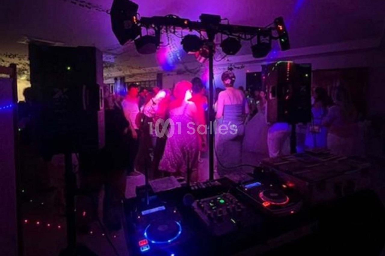 Salle de fête avec une piste de danse éclairée par des lumières colorées, vue depuis une table de mixage.