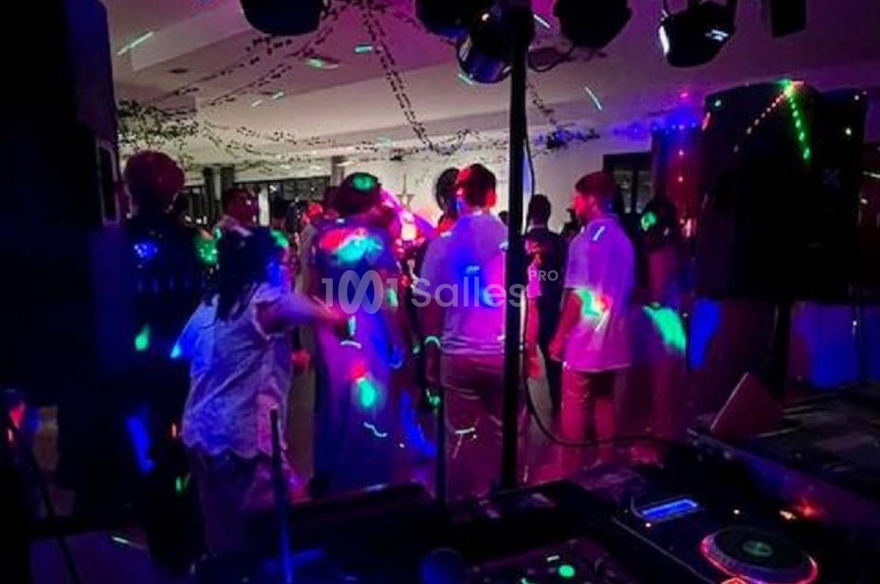 Des personnes dansent sous des lumières colorées dans une salle sombre, ambiance festive avec musique en arrière-plan.