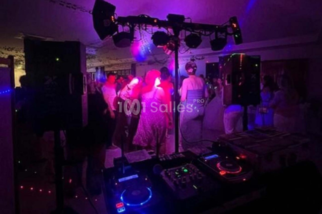 Des personnes dansent sous des lumières colorées lors d'une soirée avec une table de mixage et des enceintes au premier plan.