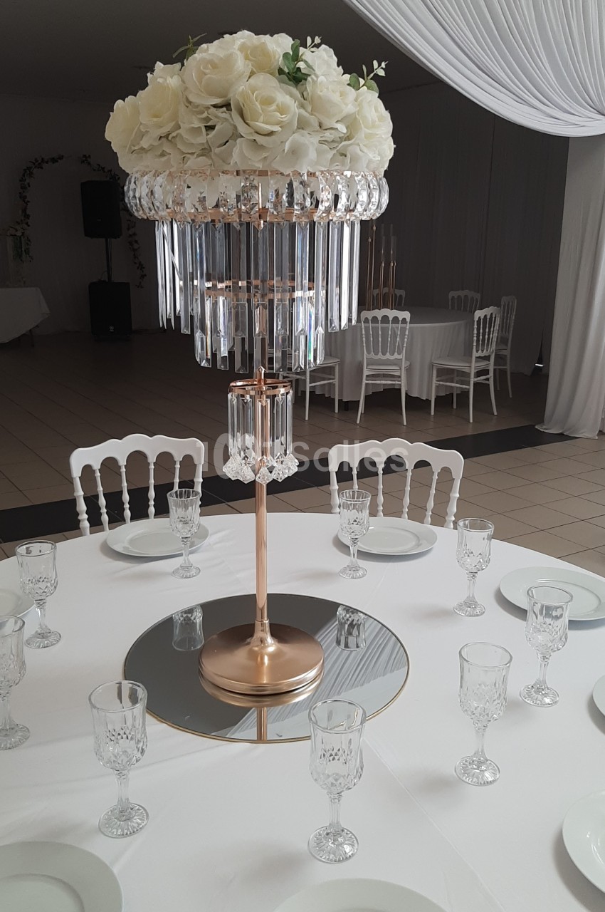 Centre de table élégant avec des roses blanches et des pampilles en cristal, entouré de vaisselle sur une nappe blanche.