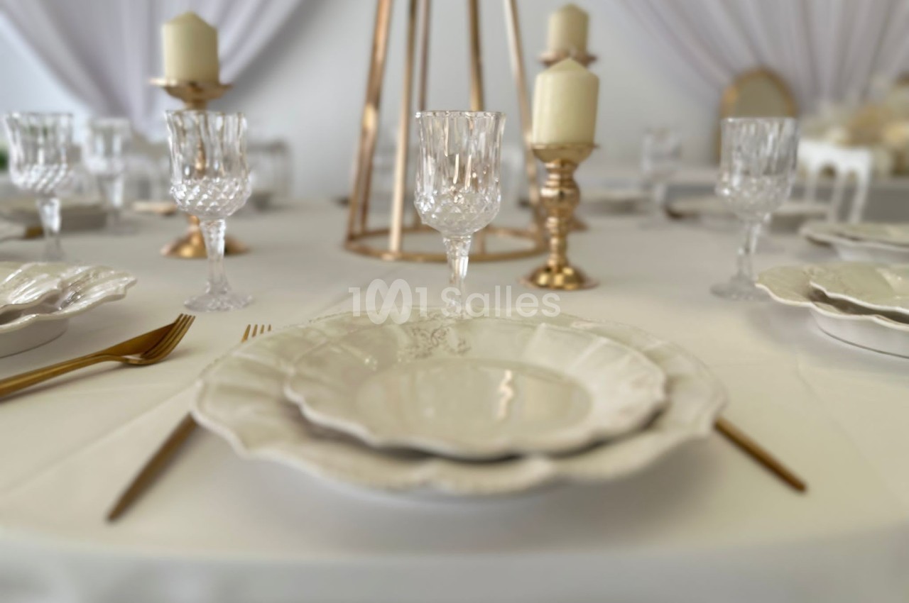 Table élégamment dressée avec vaisselle blanche, verres en cristal, couverts dorés et chandeliers décoratifs.
