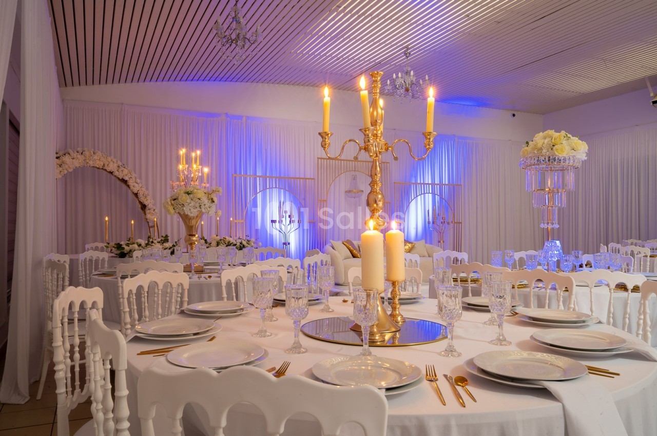 Salle de réception élégante décorée avec des chandeliers dorés, des fleurs blanches et des tables dressées.