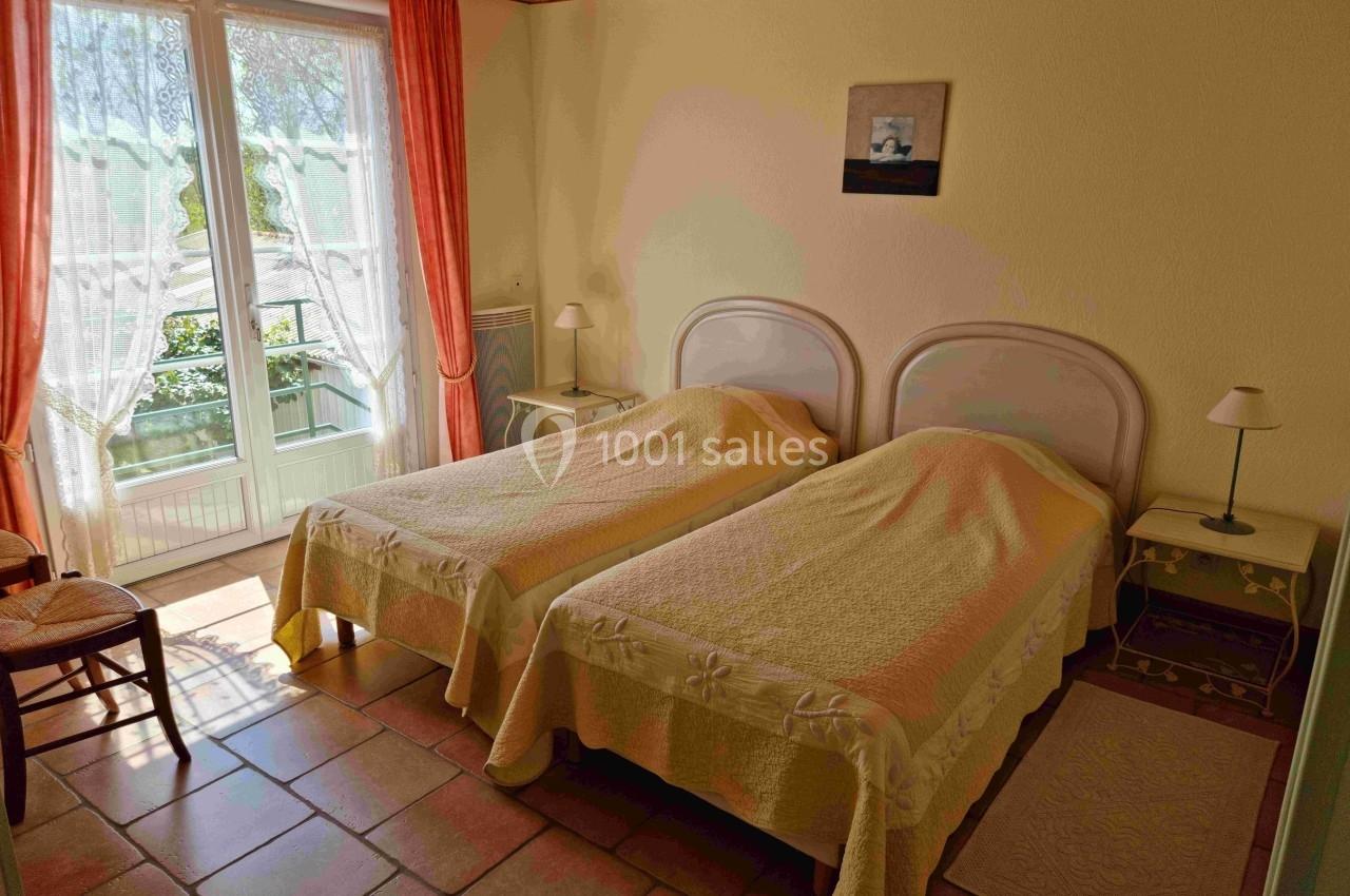 Deux lits simples avec couvre-lits jaunes dans une chambre lumineuse avec fenêtre donnant sur un balcon.