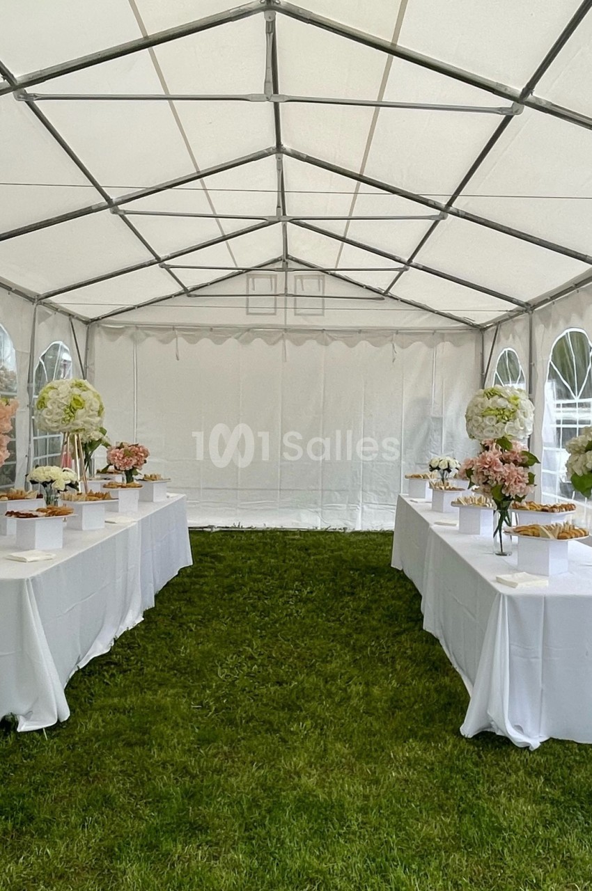 Intérieur d'une tente blanche avec des tables décorées de fleurs et de plats, posées sur une pelouse verte.