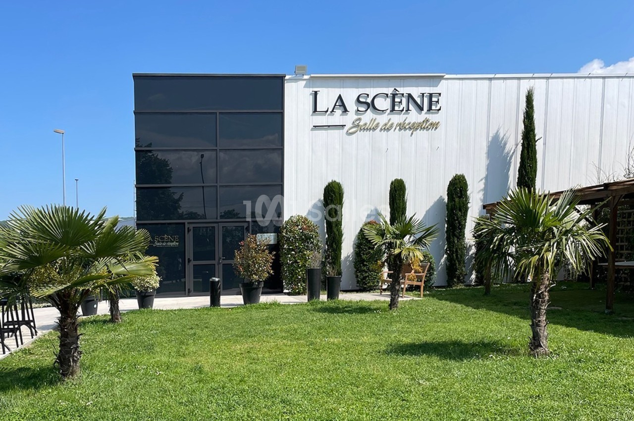 Façade d'une salle de réception moderne avec pelouse, palmiers et arbustes devant l'entrée vitrée.