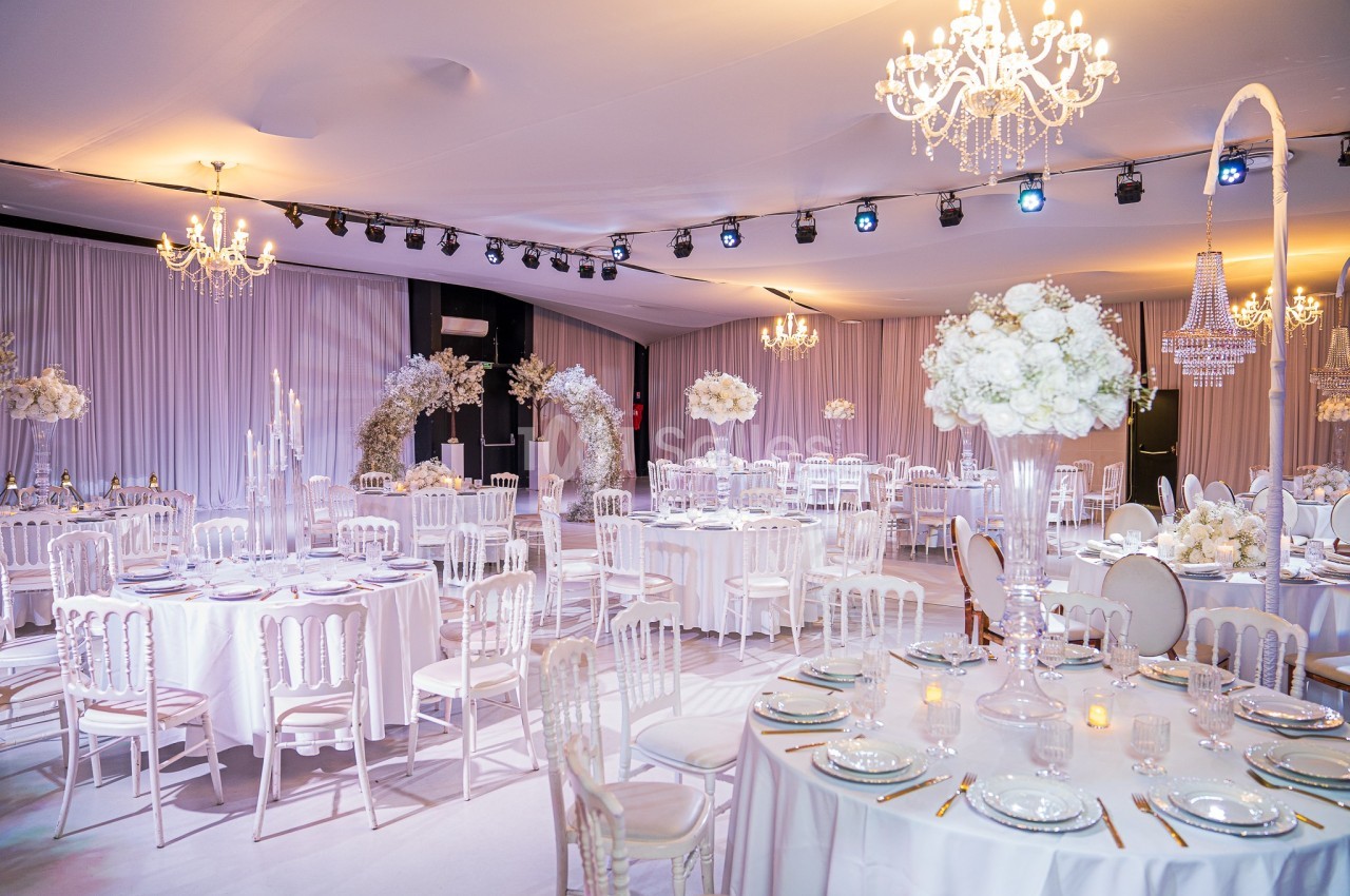 Salle de réception élégante décorée de tables rondes avec nappes blanches, chandeliers et arrangements floraux.