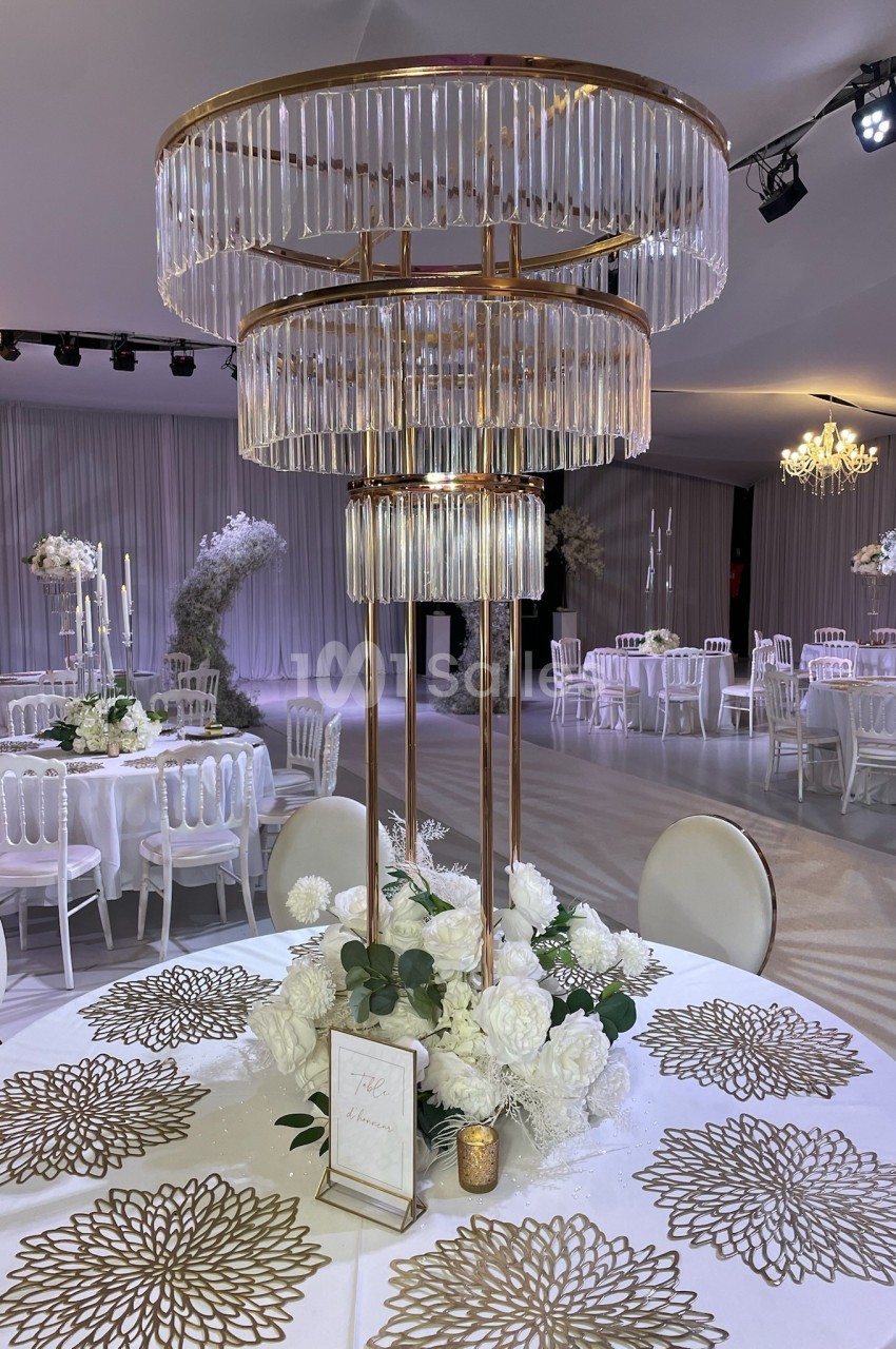 Centre de table élégant avec fleurs blanches, bougie dorée et lustre en cristal dans une salle de réception décorée.