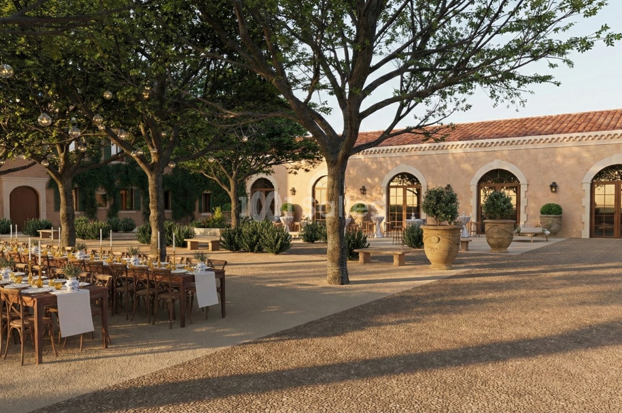 Cour extérieure aménagée avec tables dressées pour un événement, entourée d'arbres, de plantes et d'un bâtiment en pierre.