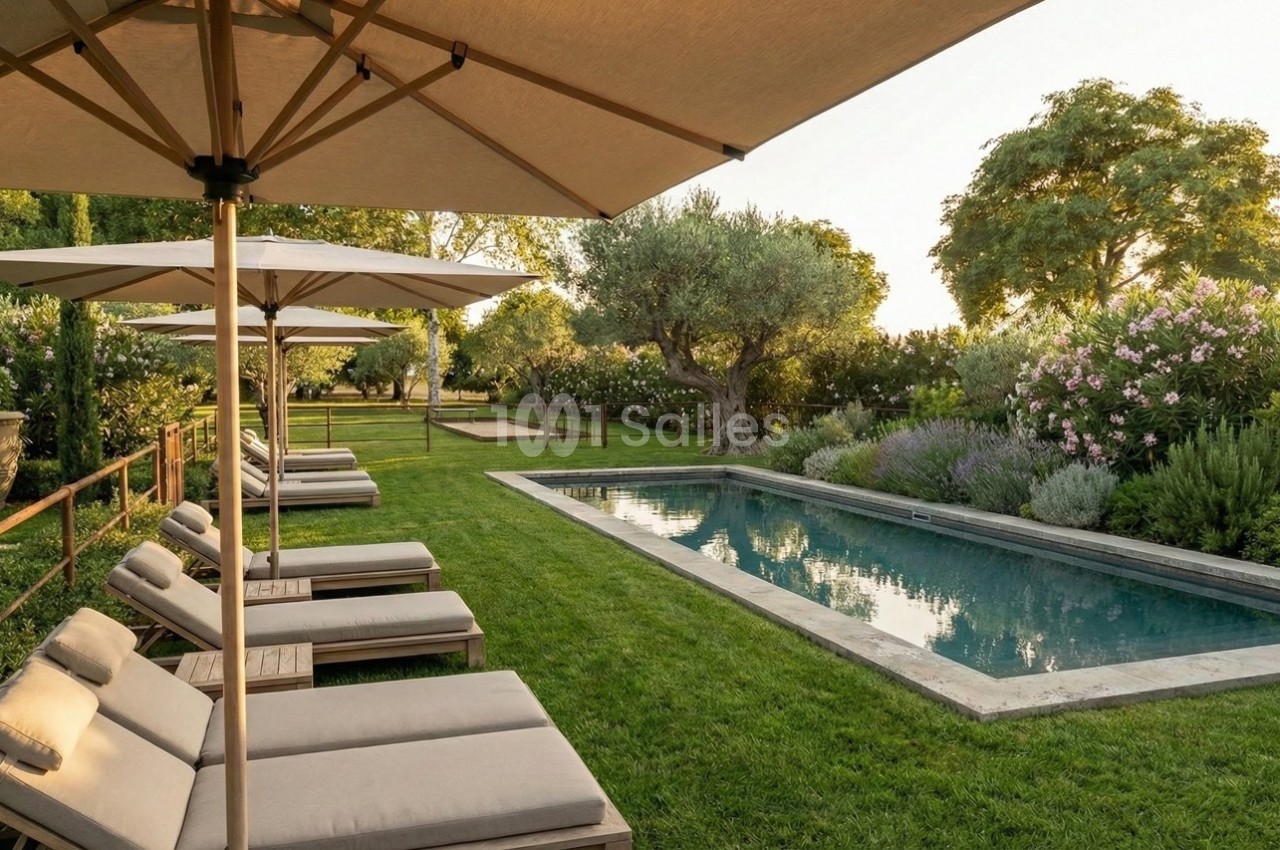 Chaises longues alignées sous des parasols près d'une piscine entourée de verdure et d'arbres au coucher du soleil.