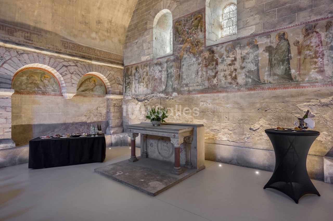 Autel en pierre dans une salle voûtée ornée de fresques murales, avec des tables dressées pour un événement.