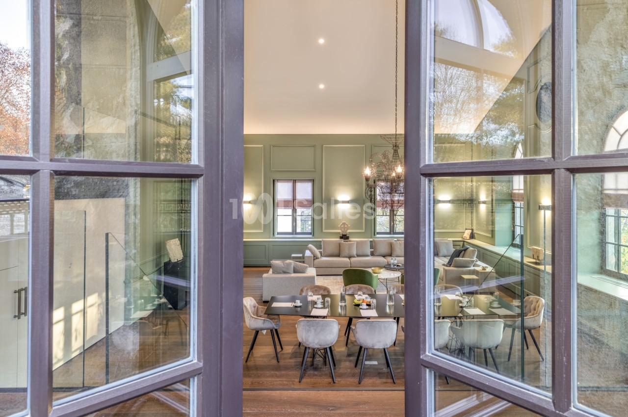 Vue à travers une porte vitrée sur une salle lumineuse avec table à manger, chaises et canapé dans un décor élégant.