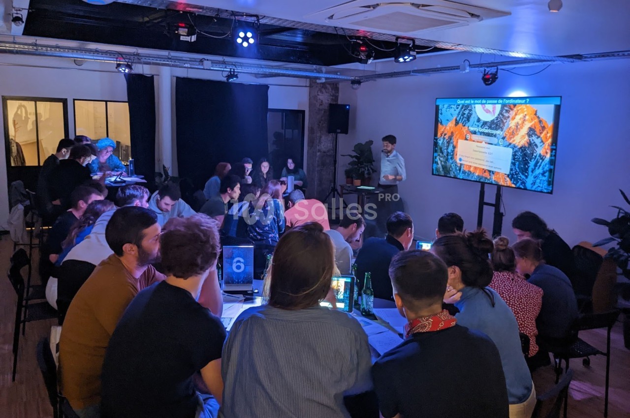 Un groupe de personnes assises autour de tables participe à une présentation projetée sur un écran dans une salle sombre.