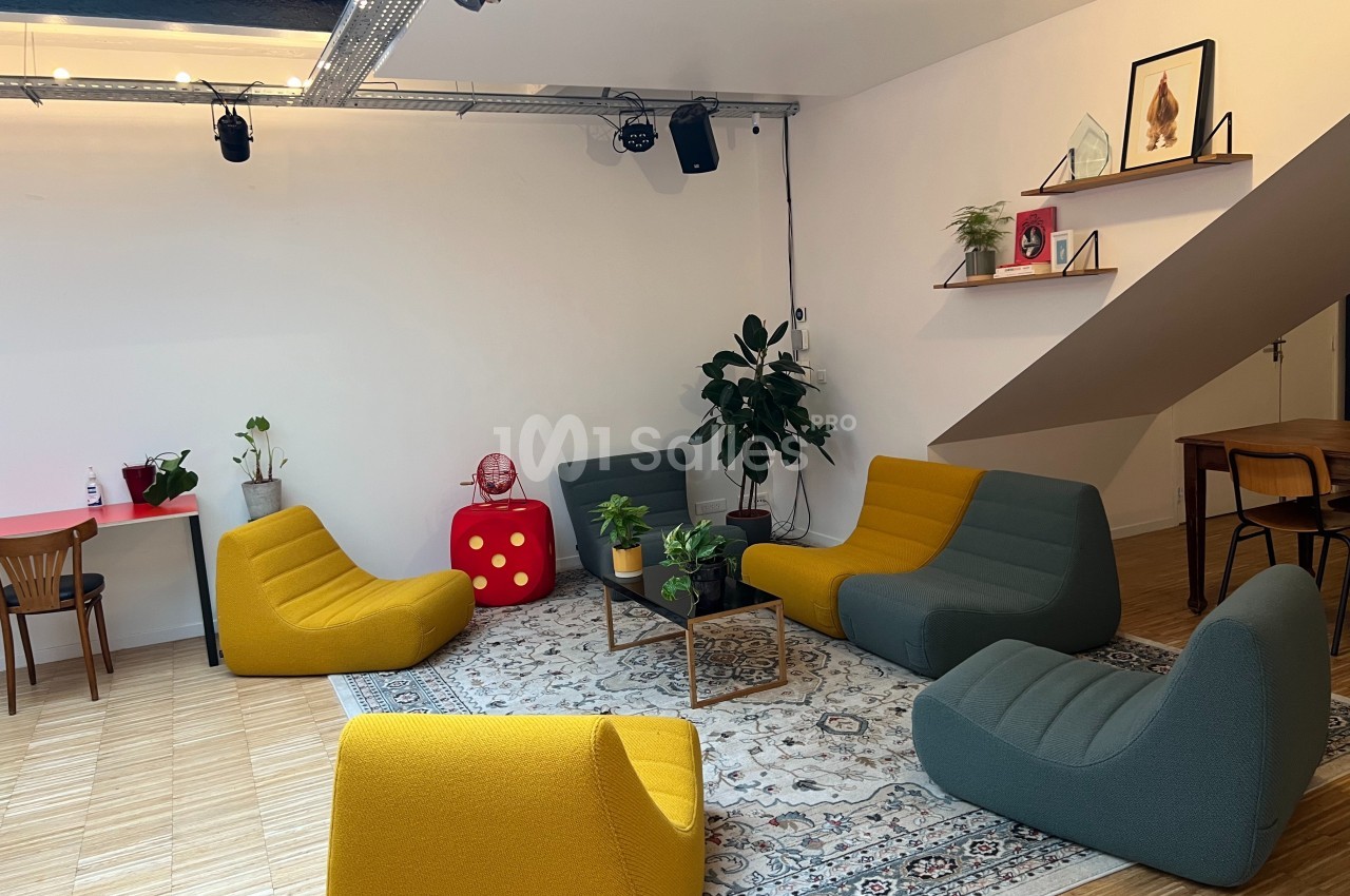 Espace de détente avec fauteuils colorés, tapis, plantes et étagères décorées dans une pièce lumineuse.
