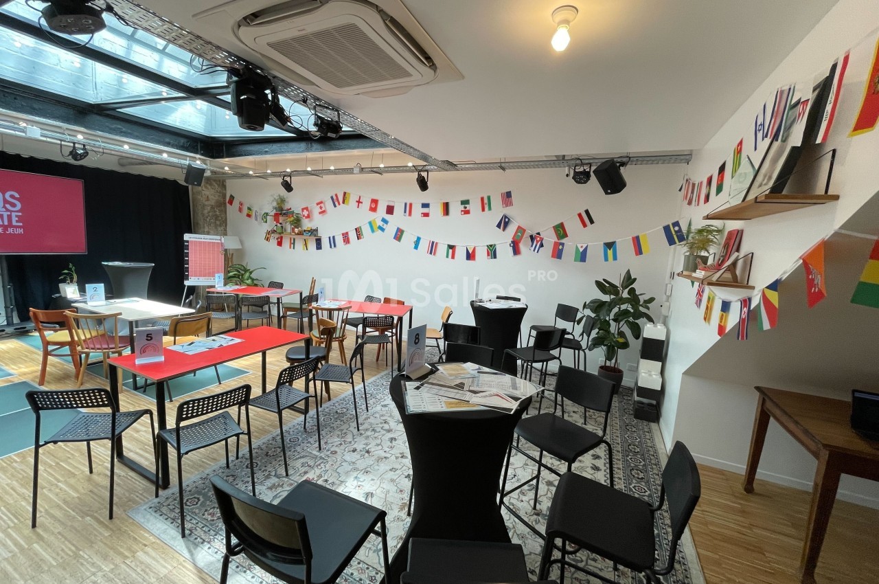 Salle lumineuse aménagée avec des tables, des chaises et des décorations de drapeaux internationaux suspendus.