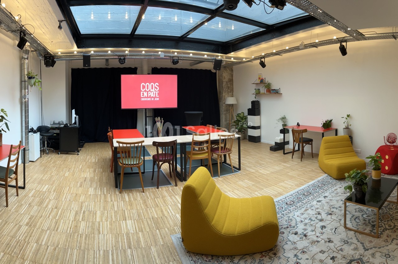 Salle lumineuse avec mobilier coloré, espace de réunion, plantes décoratives et écran affichant ’COS DIRE’.