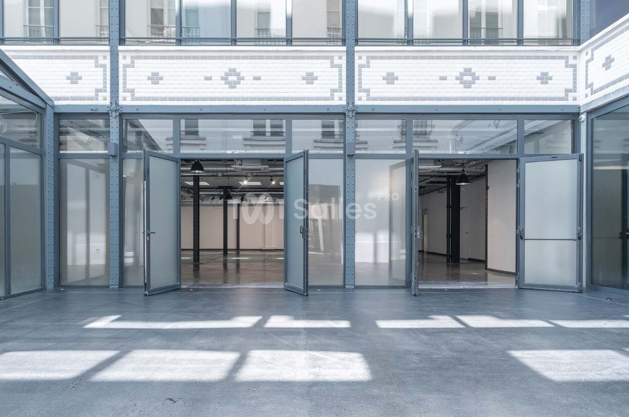 Vue d'un espace intérieur lumineux avec des portes vitrées ouvertes donnant sur une grande salle vide.