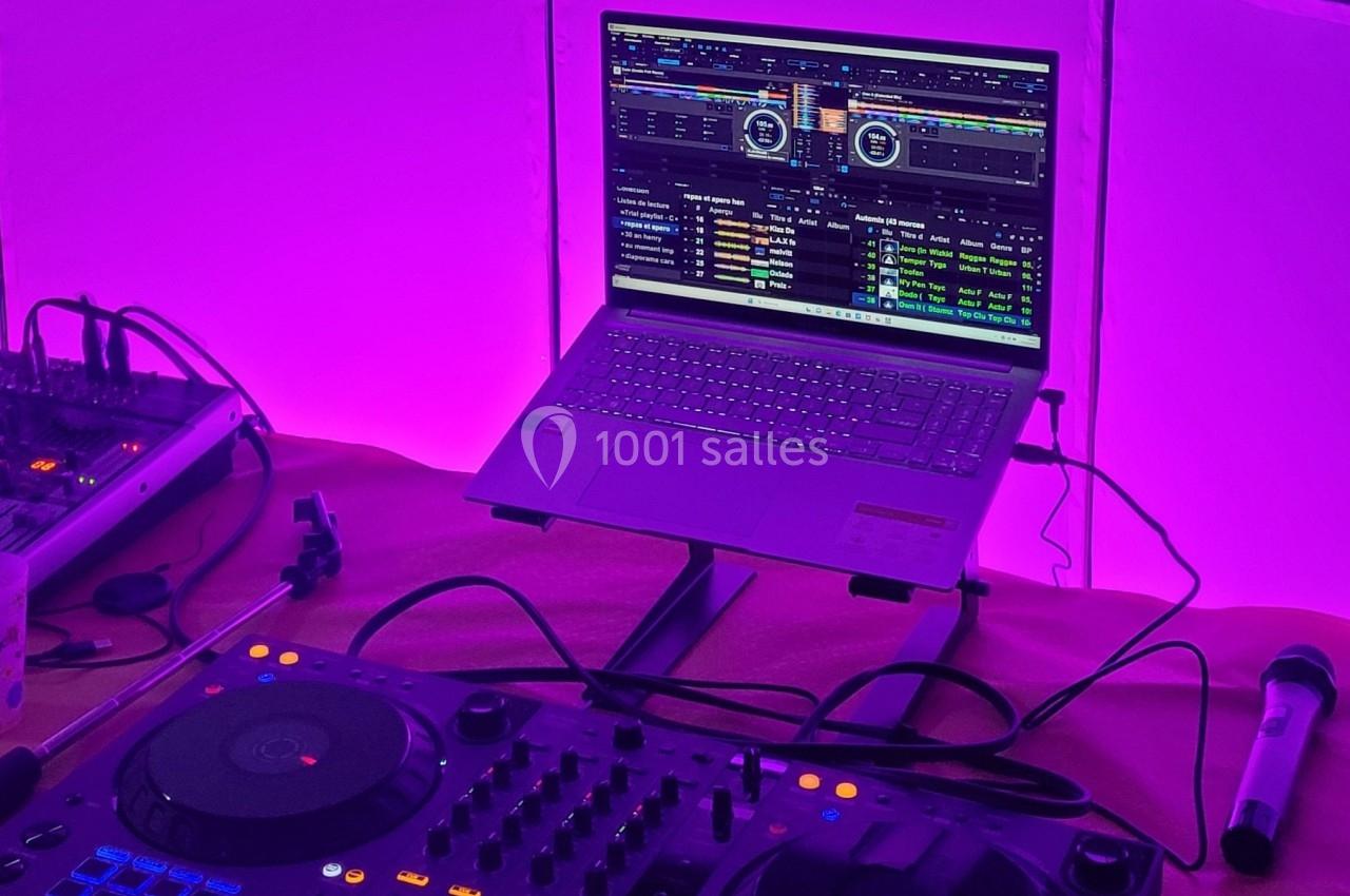 Poste de DJ avec ordinateur portable affichant un logiciel de mixage, platine et microphone sur une table éclairée en violet.