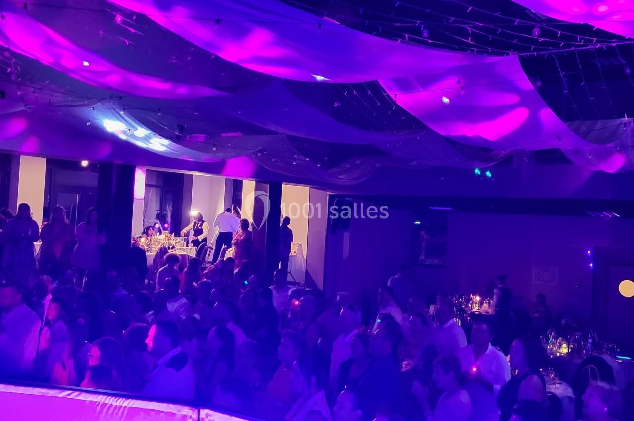 Salle de réception remplie de personnes, éclairée par des lumières violettes et décorée de voilages suspendus.