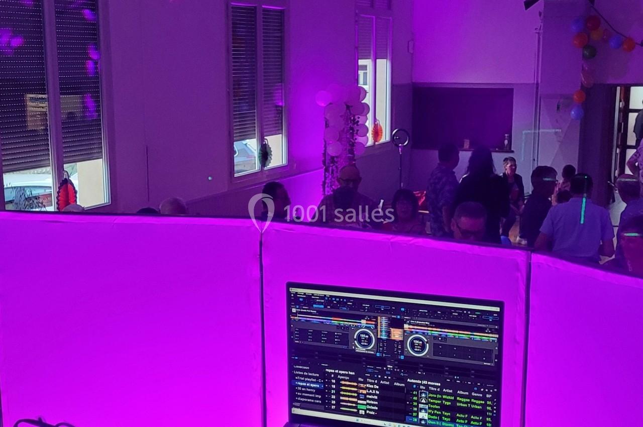 Salle de fête éclairée en violet avec des invités dansant en arrière-plan et un écran de DJ au premier plan.