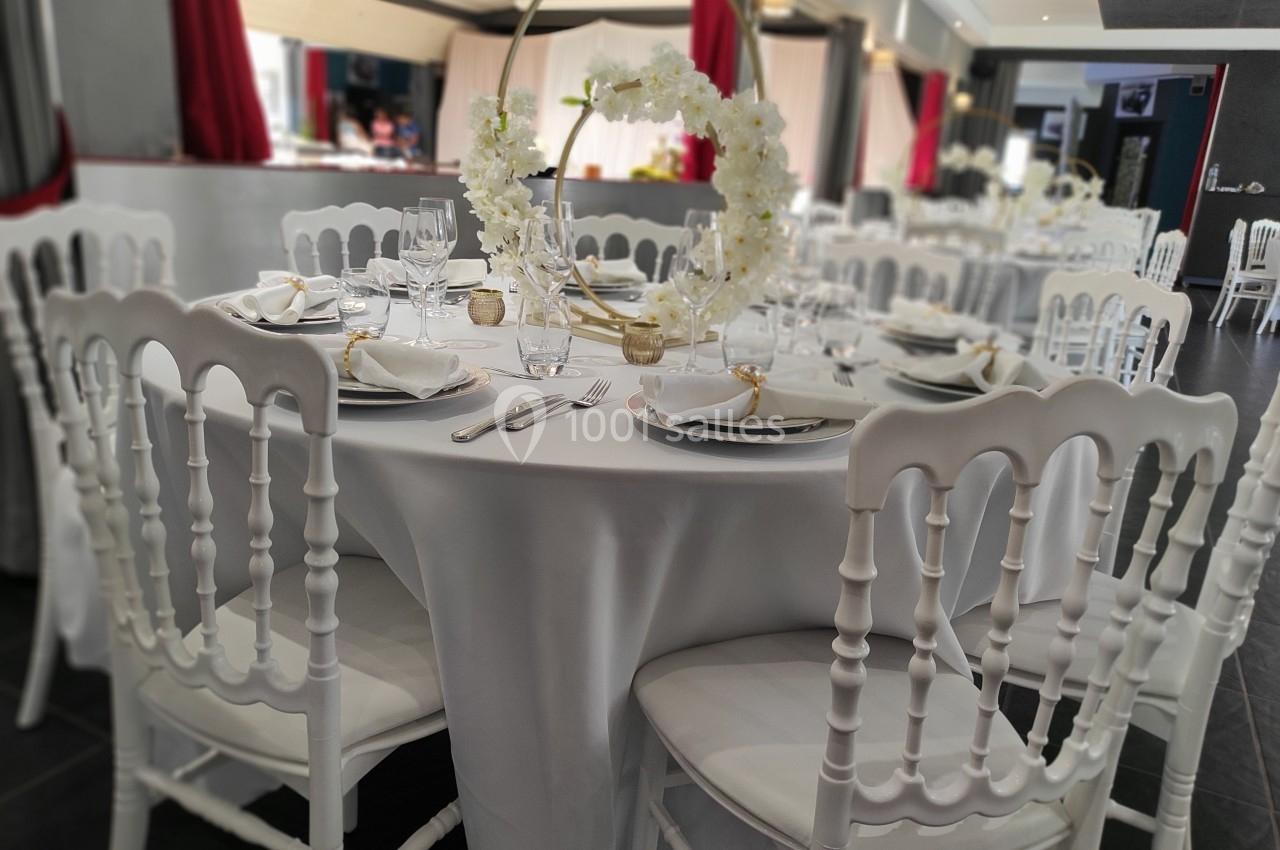 Table ronde élégamment dressée avec nappes blanches, chaises assorties et centre de table floral dans une salle de réception.