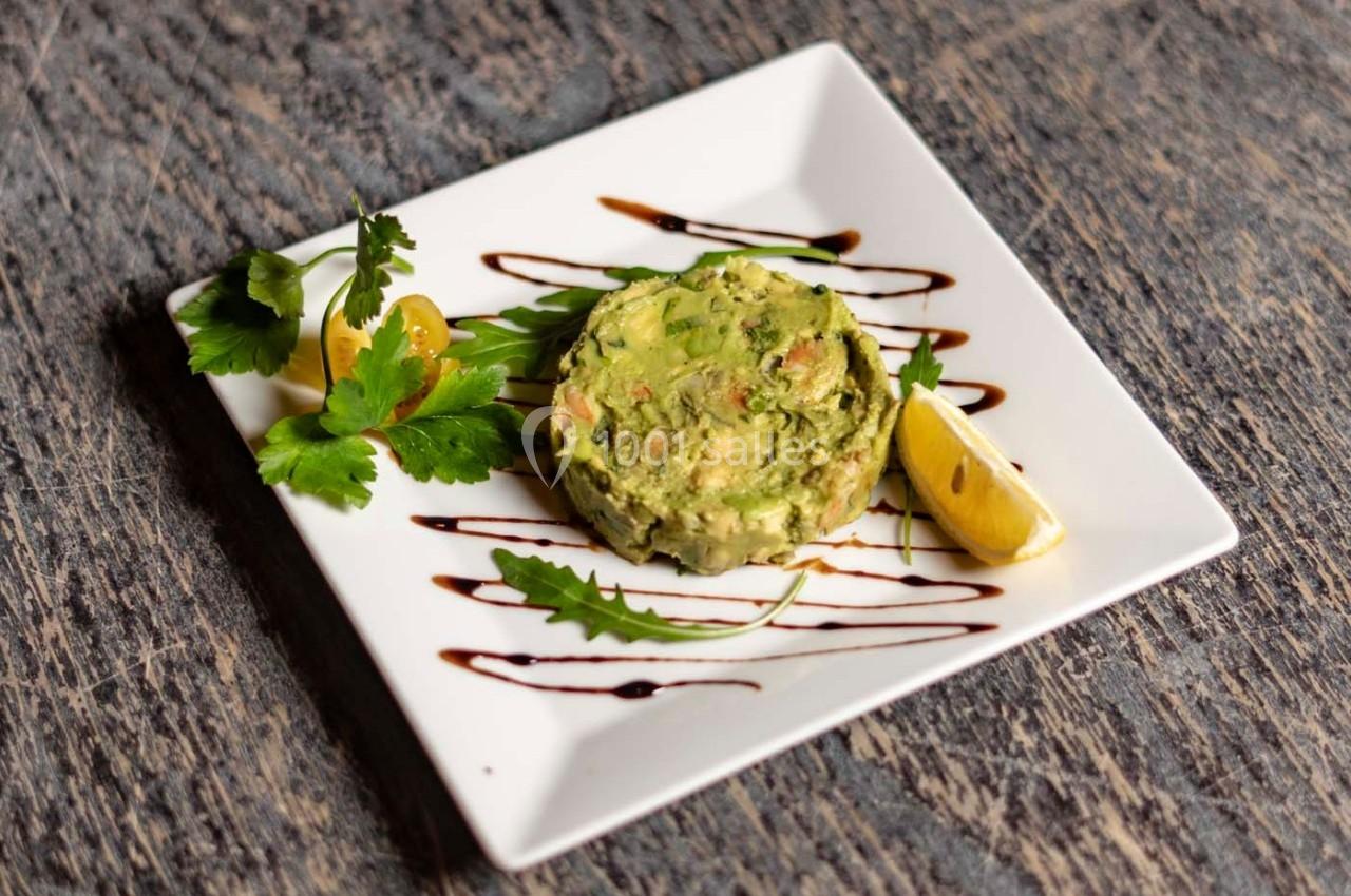 Tartare d'avocat avec herbes fraîches, citron et filet de sauce balsamique, présenté sur une assiette carrée blanche.