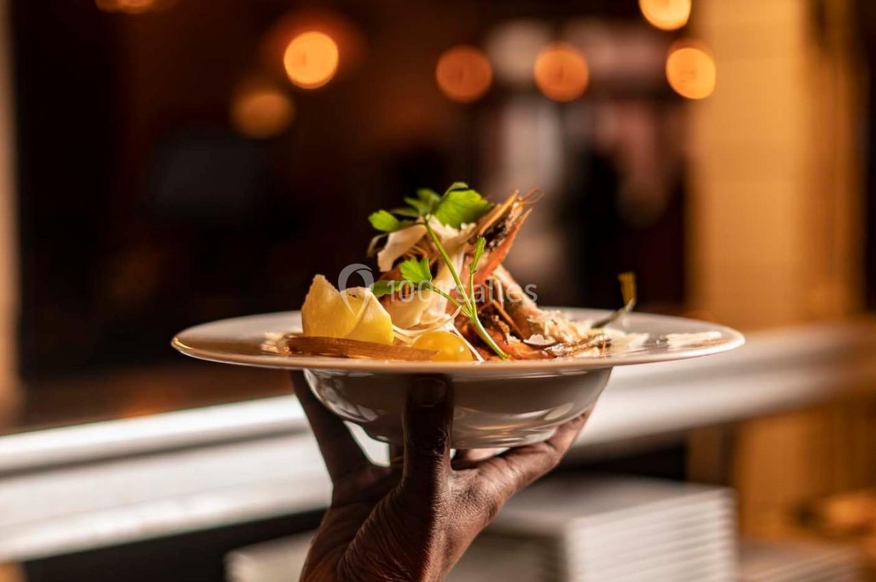 Assiette de fruits de mer garnie de citron et herbes fraîches, tenue par une main dans un restaurant éclairé.